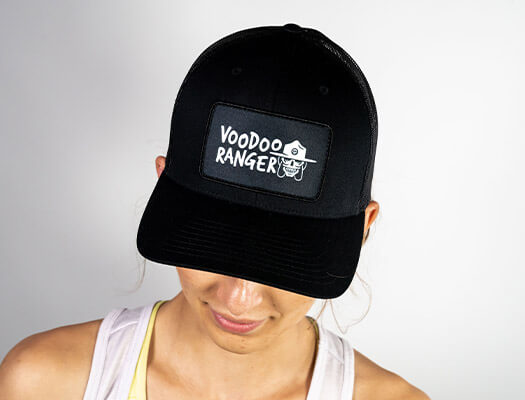 Female model wearing the hat. The front of the hat has a patch that says "Voodoo Ranger" and has an image of the Voodoo Ranger character's head.