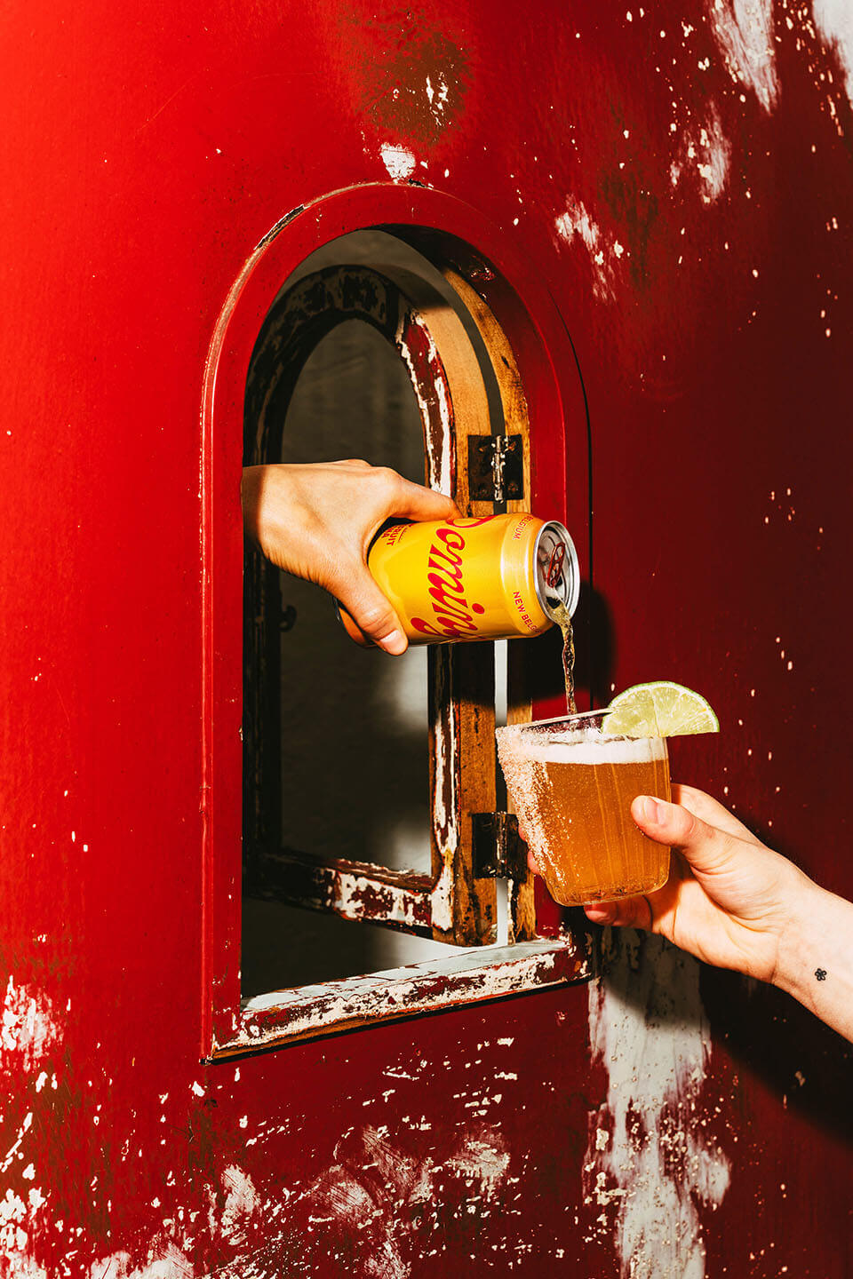 Hand pouring can of Dominga into a glass garnished with salt and a lime. 